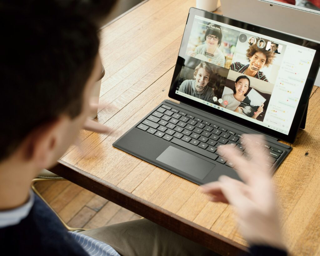 Photo of a person doing remote work at a laptop displaying a video call with four other people